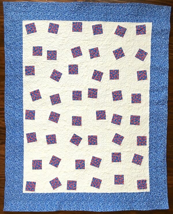 Baby quilt featuring Red floral fabric set into white background with blue borders