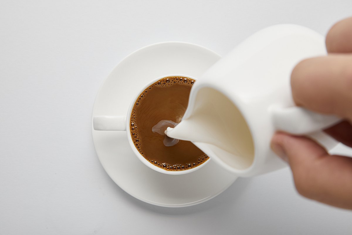 Person pouring cream into coffee