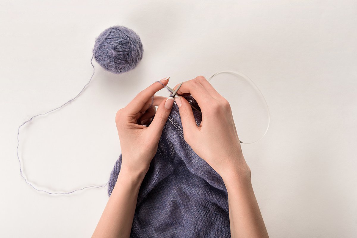 Person knitting something with plum-colored yarn