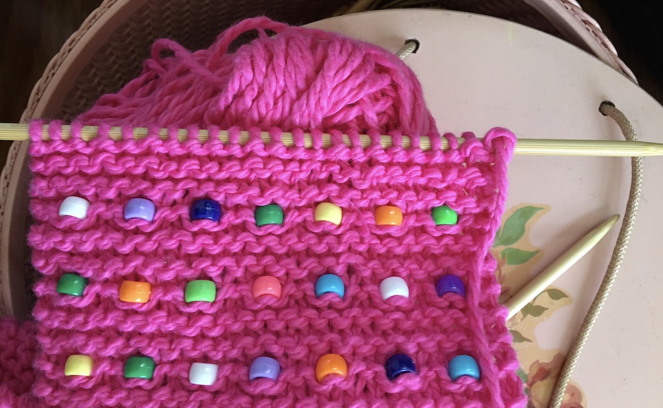 Pink knitted scarf with beads laying on sewing basket