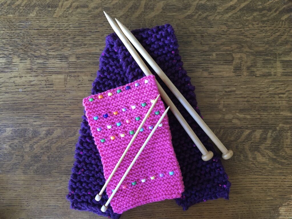Pink knitted scarf and purple knitted scarf and knitting needles