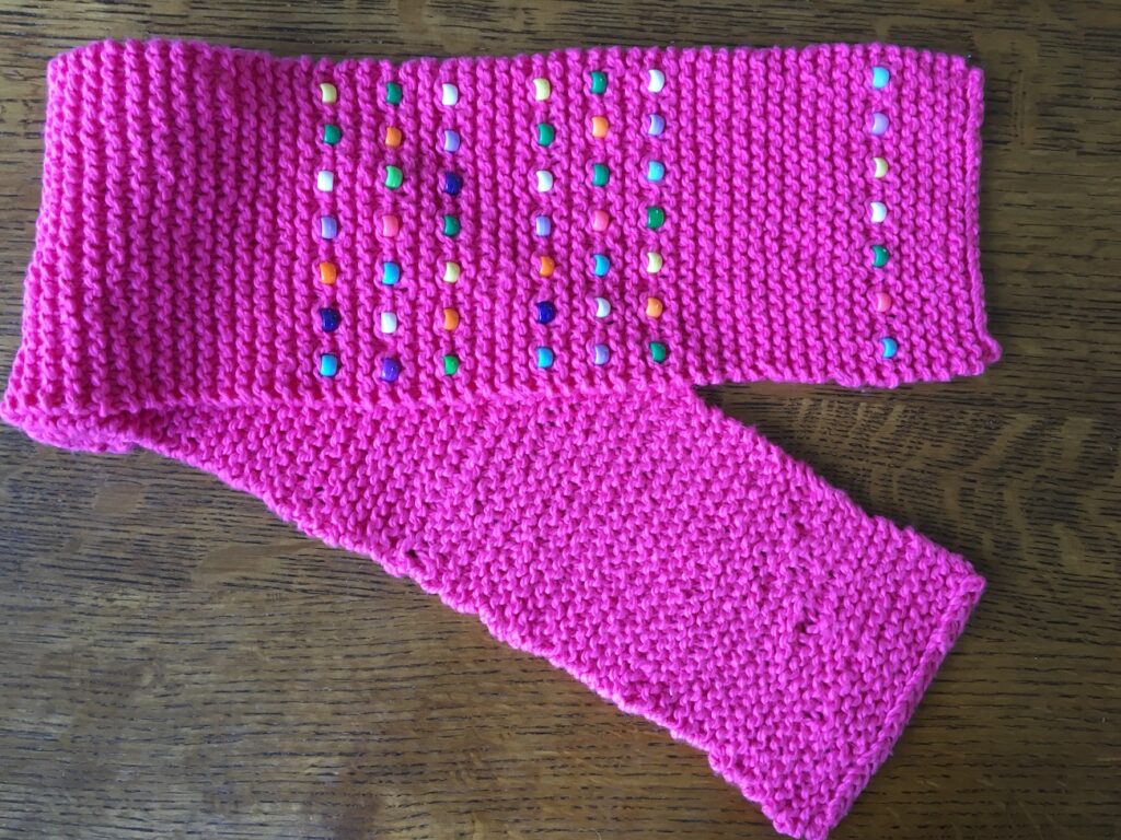 Knitted pink scarf with brightly-colored plastic beads