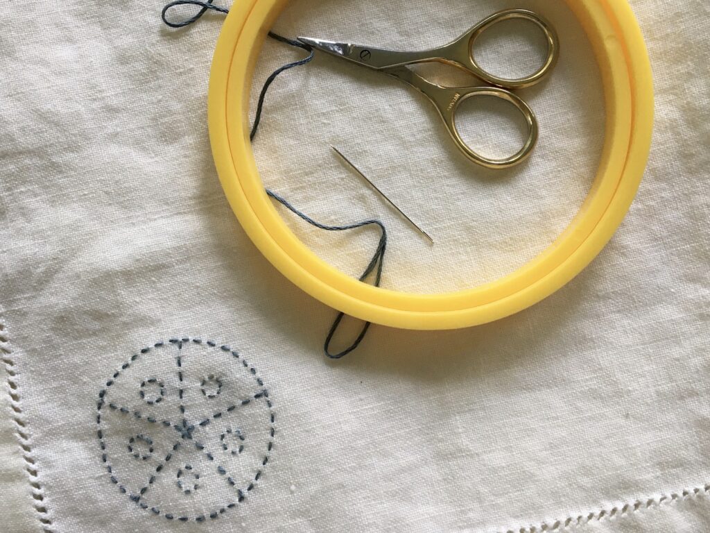 Circle Embroidery Pattern Stitched in Blue Thread on White Linen Napkin and hoop, thread, scissors, and needle